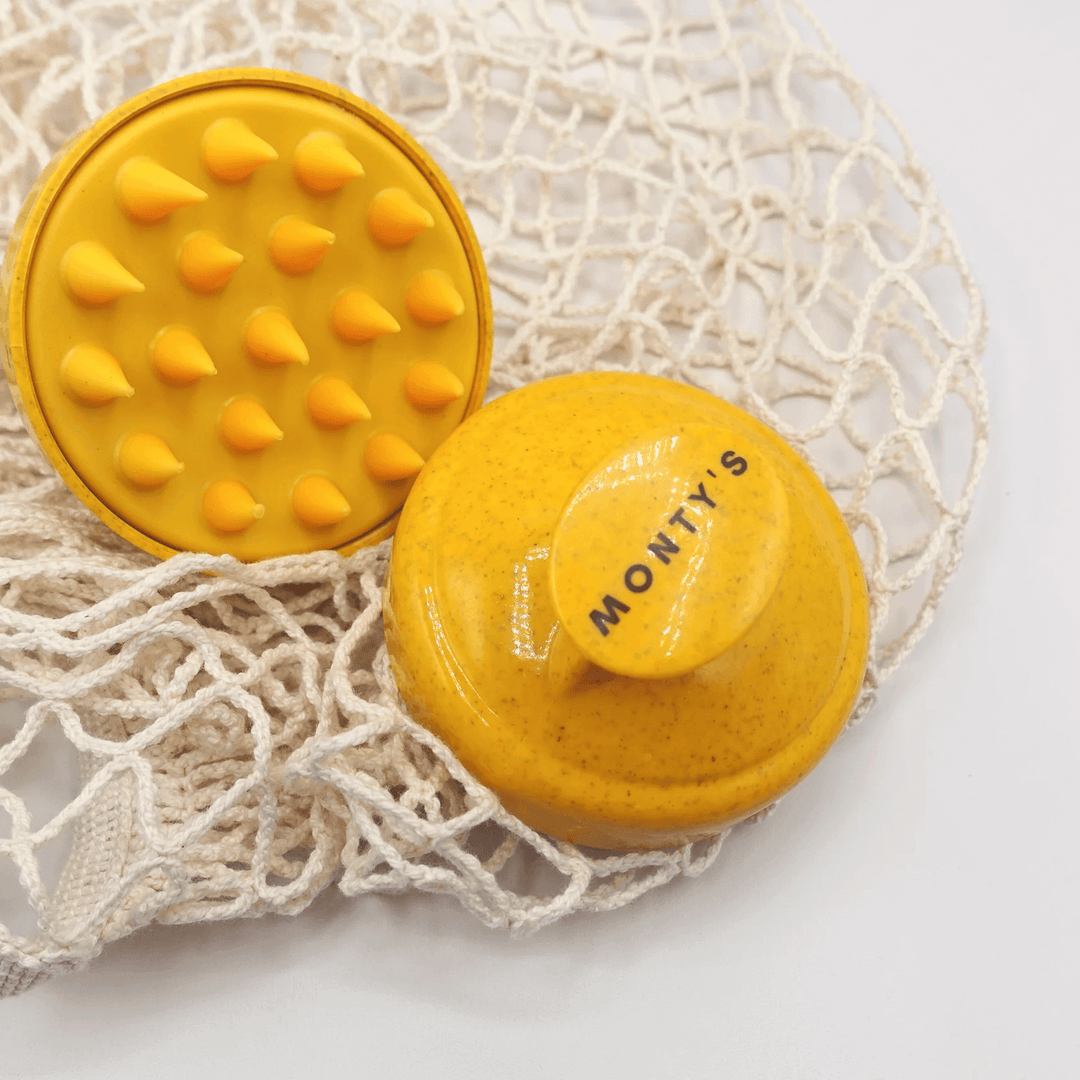 Monty's yellow dog shampoo brush with soft bristles and ergonomic handle, placed on a natural net for eco-friendly pet grooming.