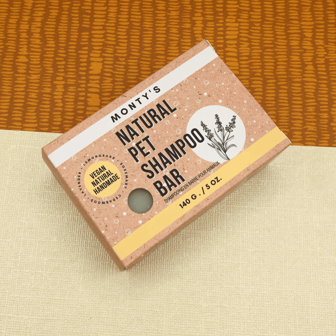 Monty's Natural Pet Shampoo Bar, vegan and handmade, 140g box with natural design, placed on beige and orange fabric background.