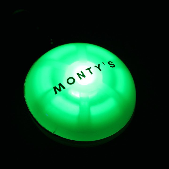 Rechargeable green LED dog tag light glowing in the dark with "Monty's" label for pet night safety.