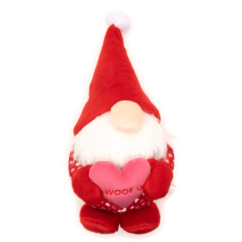 A festive dog toy in the shape of a gnome with a plush red hat and a long white beard. The toy is holding a red heart with the words 'WOOF U' in the center, conveying a message of love and playfulness. It has a soft, cuddly texture, and the white background of the image accentuates the bright red color and the whimsical design of the toy, making it an appealing gift for a pet during the holiday season.