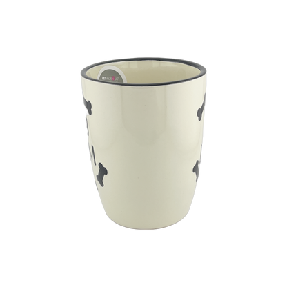 A ceramic mug with a white base and black rim, displaying small black bone shapes around the exterior. The mug has a simple and minimalist design, highlighting the bone patterns against the white background.