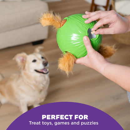 Person inserting Puzzle Bitez treats into a green dog toy while a dog waits in the background, showing use for treat toys and games.