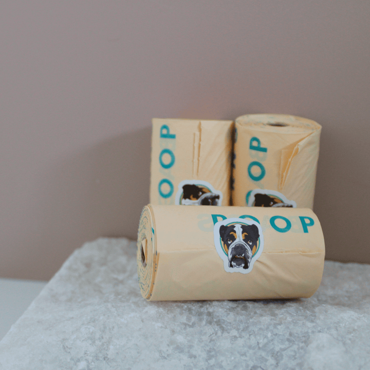 Three rolls of Monty's compostable poop bags with dog illustrations, placed on a stone surface, designed for eco-friendly pet waste disposal.