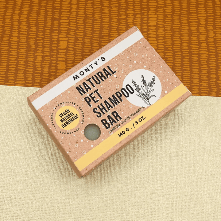 Monty's Natural Pet Shampoo Bar, vegan and handmade, 140g box with natural design, placed on beige and orange fabric background.