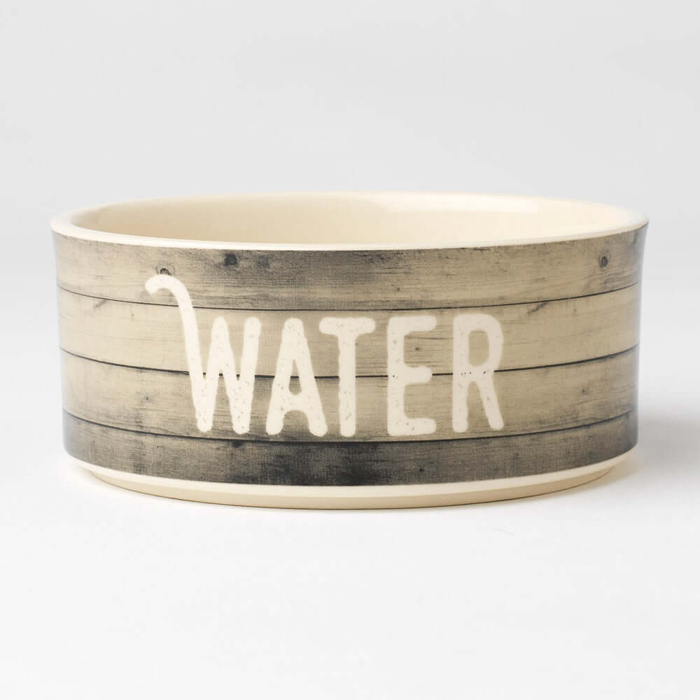 A beige stoneware bowl with a rustic wood plank pattern and the word 'WATER' printed in black. It has a bone-shaped graphic in the basin.