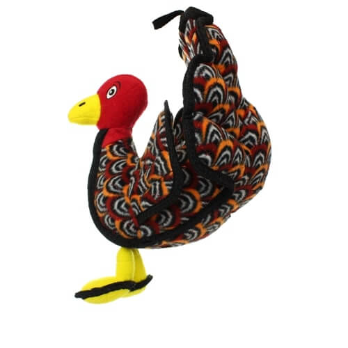 Side view of a plush turkey-shaped dog toy with a red head, yellow beak, and colorful patterned feathers in black, orange, and white.