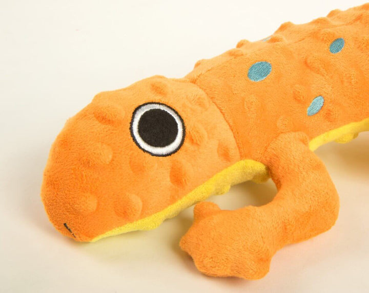 Close-up of an orange plush lizard-shaped dog toy with black and white eyes, blue spots, and a yellow underside, designed for interactive play.