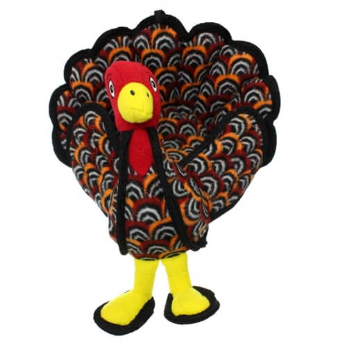 Plush turkey-shaped dog toy with a red head, yellow beak, and yellow feet, featuring colorful patterned feathers in black, orange, and white.